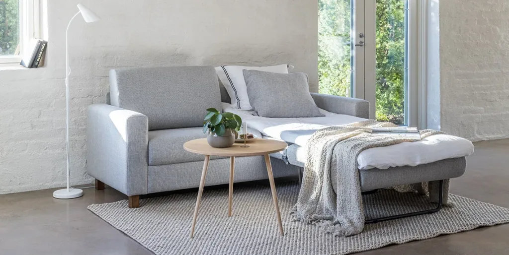Vaaleanharmaa Fox kolmen istuttava vuodesohva, jonka edessä sohvapöytä. Vuodesohvan toinen puoli vuoteesta avattuna ja pedattuna kevyt petauspatjalla.