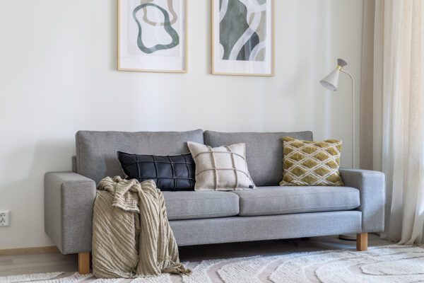 Kolmen istuttava Studio-sohva verhoiltuna vaaleanharmaalla kankaalla. Sohvalla tyynyjä ja viltti.
