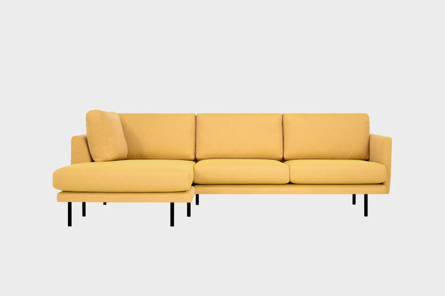 Kanerva-avokulmasohva verhoiltuna keltaisensävyisellä kankaalla ja jalkoina mustat pyöreät metallijalat, tuotekuva edestäpäin kuvattuna, jossa divaani vasemmalla.