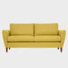 KUURA-sohva-2-5ist-180x85cm-stark618-pahkina-Finsoffat Leveämpi 2 hengen Kuura-sohva keltaisella kankaalla verhoiltuna ja jalkoina pähkinän väriset puujalat kuvattuna suoraan edestäpäin harmaata taustaa vasten.