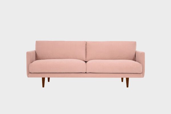 Vaaleanpunainen kolmen hengen sohva, jossa ruskeat puujalat.