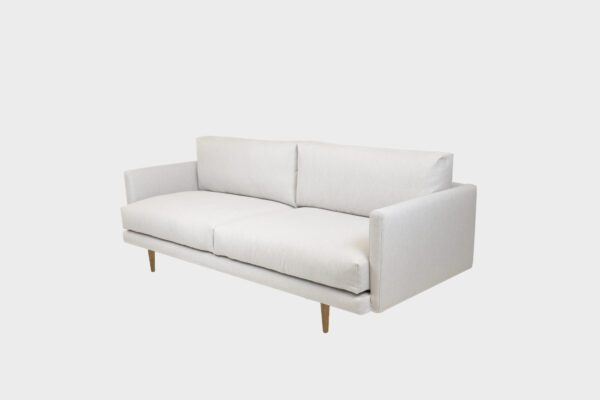 Havu 3-istuttava sohva verhoiltuna vaalealla kankaalla ja aitotammen väriset jalat, tuotekuva kuvattuna viistosta.