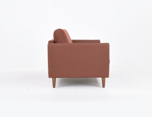 Kuura-3 istuttava sohva punertavalla kankaalla verhoiltuna ja jalkana pähkinä puujalka, tuotekuva sivusta kuvattuna.