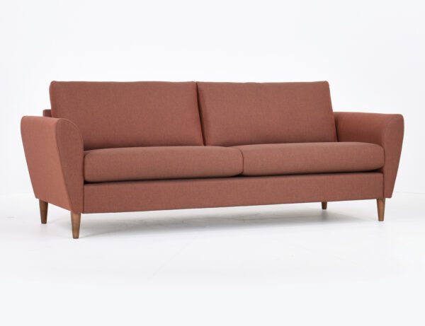 Kuura-3 istuttava sohva punertavalla kankaalla verhoiltuna ja jalkana pähkinä puujalka, tuotekuva viistosti kuvattuna.