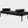 Siesta-daybed verhoiltuna tummalla kankaalla, somisteena kaksi tyynyä ja jalkoina metallijalat, tuotekuva viistosti kuvattuna.
