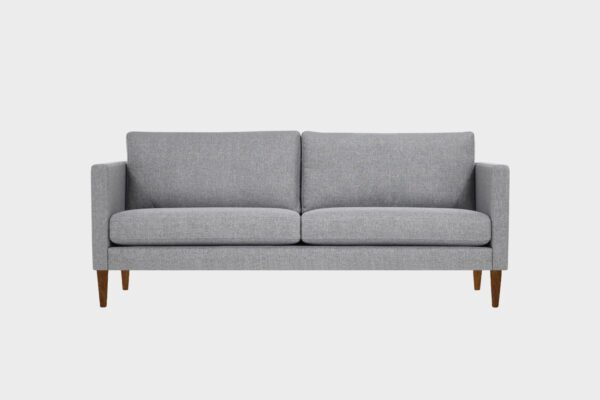 Tuohi-3 istuttava sohva harmaalla kankaalla verhoiltuna ja jalkana pähkinänsävyiset puujalat, tuotekuva edestäpäin kuvattuna.