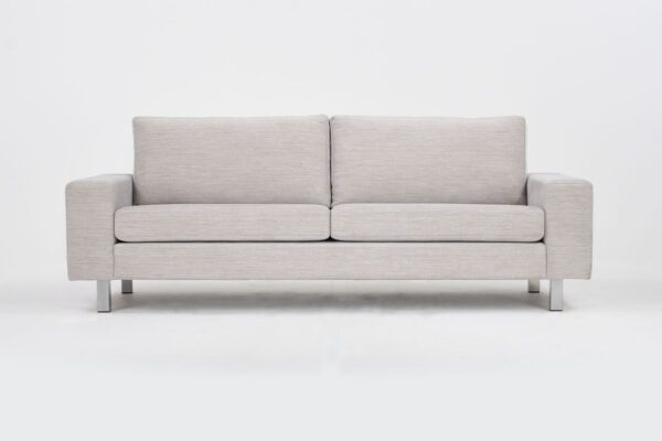 Studio 3 istuttava sohva vaalealla kankaalla verhoiltuna ja jalkana kantikkaat metallijalat, tuotekuva edestäpäin kuvattuna.