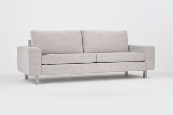 Studio 3 istuttava sohva vaalealla kankaalla verhoiltuna ja jalkana kantikkaat metallijalat, tuotekuva viistosti kuvattuna.