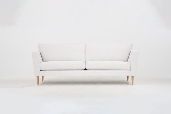 Valkoinen kolmen istuttava sohva tammijaloilla.