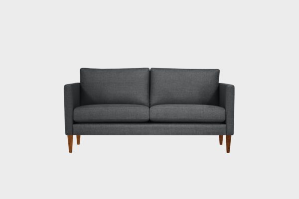 Tumman harmaa 2,5 istuttava sohva pähkinän värisin jaloin edestäpäin kuvattuna.