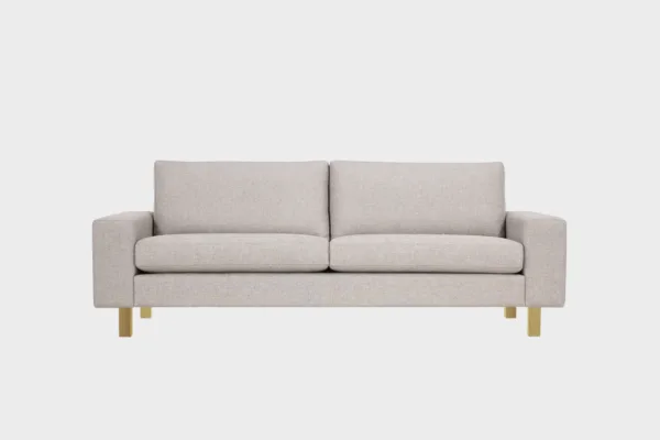 Vaalean beige 3n istuttava Studio XL -sohva tammen värisillä jaloilla kuvattuna suoraan edestäpäin vaaleaa taustaa vasten.
