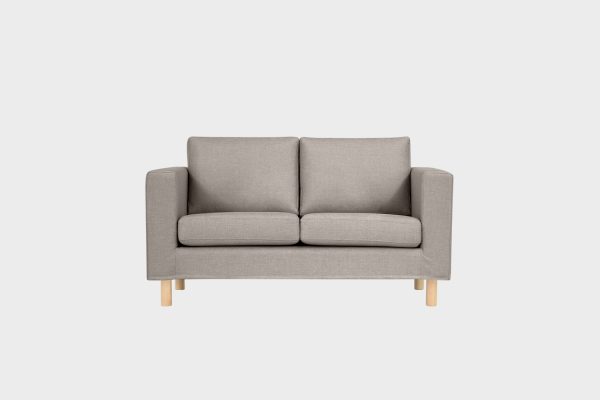 Vaaleanruskea kahden istuttava sohva koivun värisillä jaloilla kuvattuna suoraan edestäpäin.