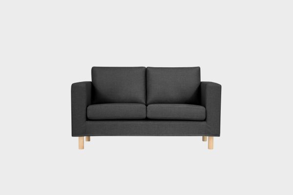 Tummanharmaa kahden istuttava sohva koivun värisillä jaloilla kuvattuna suoraan edestäpäin.