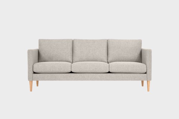 Beigellä kankaalla verhoiltu 3 istuttava sohva 3lla tyynyllä, jossa tammenväriset puujalat.