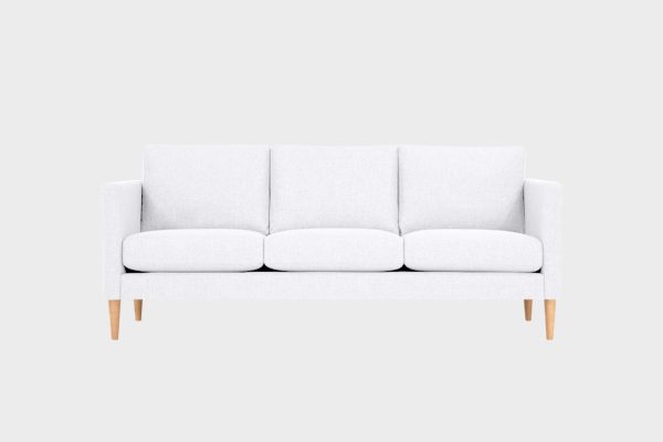 Valkoisella kankaalla verhoiltu 3 istuttava sohva 3lla tyynyllä, jossa tammenväriset puujalat.
