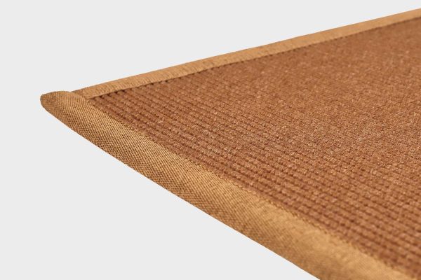 Kuparin värinen VM Carpet Esmeralda matto. Lähikuva maton kulmasta, josta näkyy kanttaus ja maton materiaali.