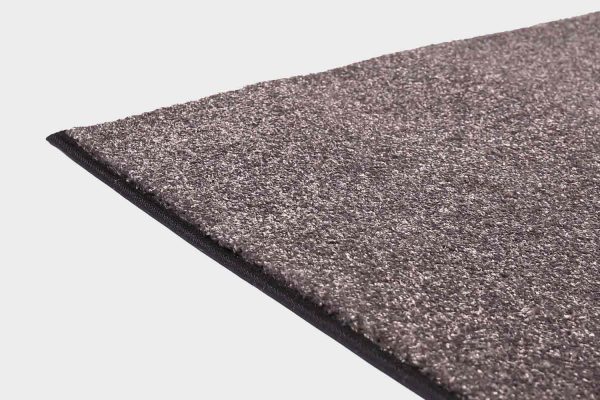 Tummanharmaa VM Carpet Hattara matto. Lähikuva maton kulmasta, josta näkyy kanttaus ja maton materiaali.