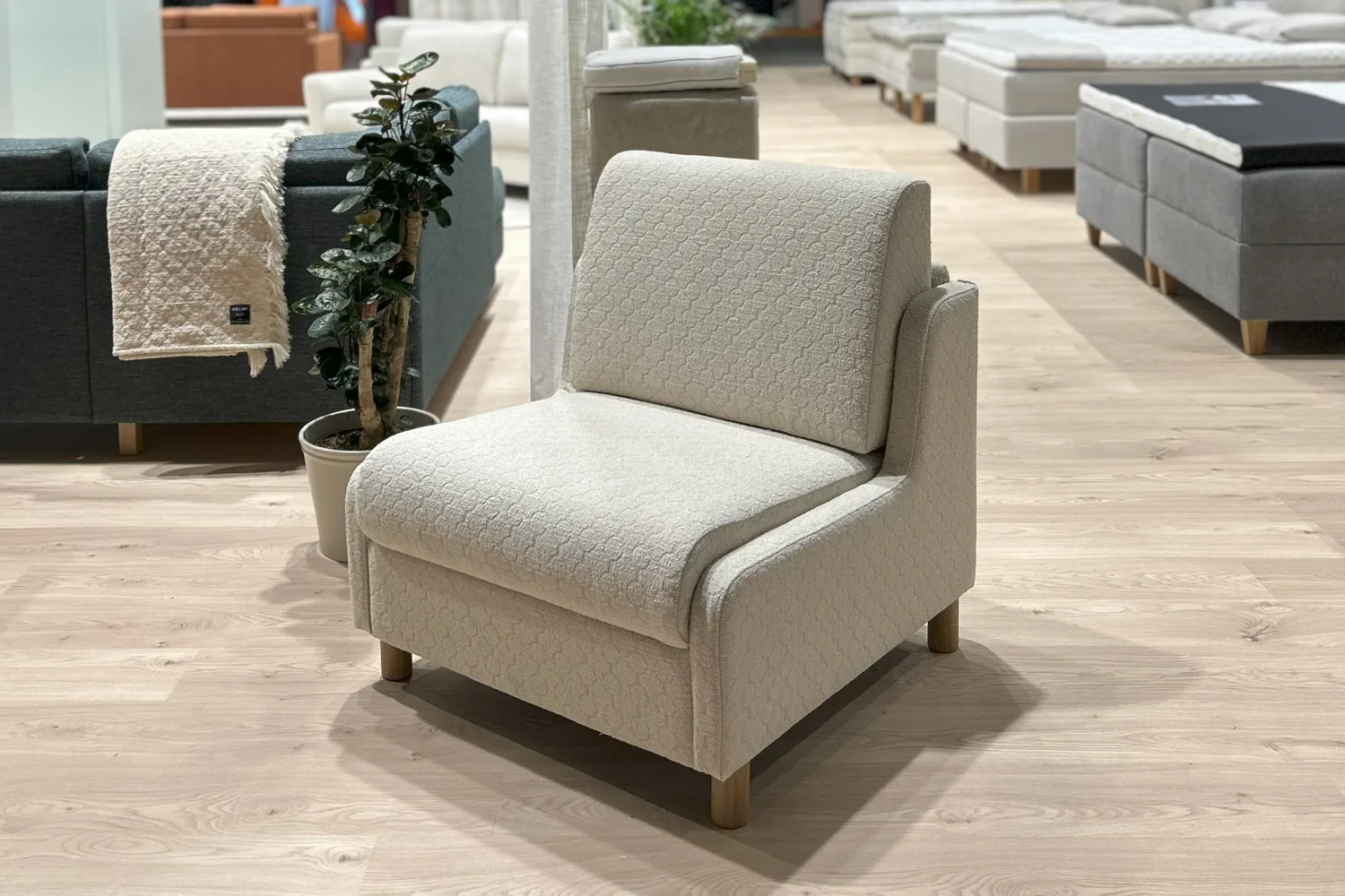 Luonnonvalkoinen vuodetuoli tammisin jaloin kuvattuna viistosti edestäpäin vaaleaa taustaa vasten Habitare-messuilla.