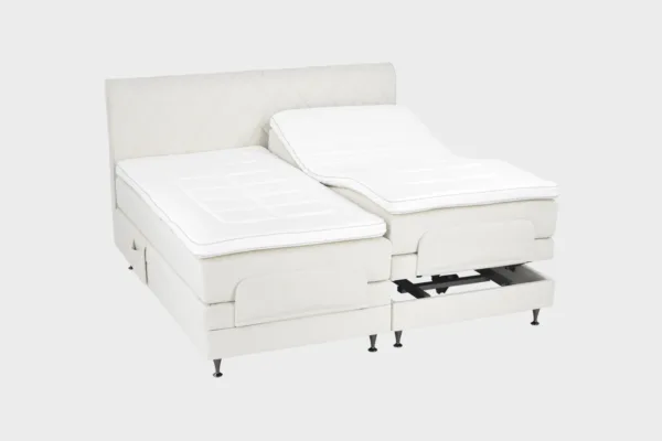 Todella vaalea moottorisänky 200x200 cm mustilla jaloilla sekä samanvärisellä sängynpäädyllä. Parisänky on kuvattuna viistosti toisen sänkypuoliskon päädyt aavistuksen koholla vaaleaa taustaa vasten.