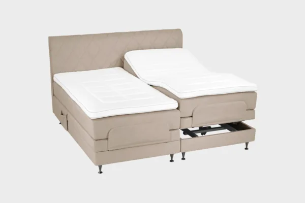 Vaalean ruskea moottorisänky 200x200 cm mustilla jaloilla sekä samanvärisellä sängynpäädyllä. Parisänky on kuvattuna viistosti toisen sänkypuoliskon päädyt aavistuksen koholla vaaleaa taustaa vasten.