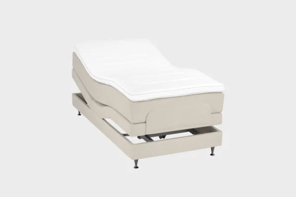 Vaalean beige moottorisänky 90x200 cm mustilla jaloilla. Yhden hengen säätösänky on kuvattuna viistosti päädyt aavistuksen koholla vaaleaa taustaa vasten.